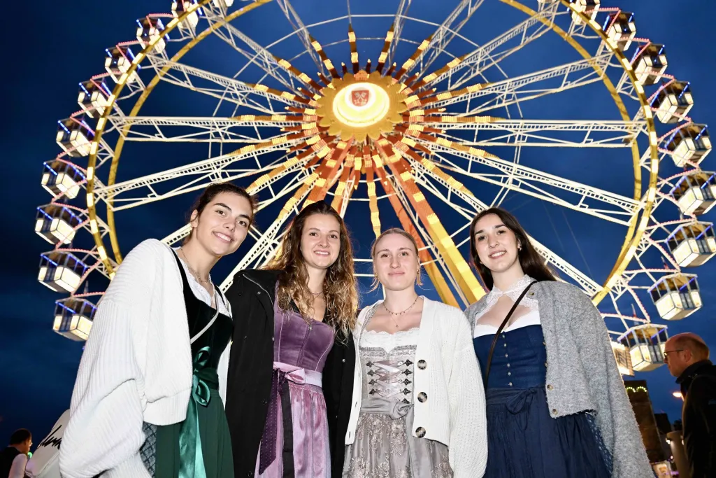 Vier junge Frauen in Dirndln posieren vor dem bunt beleuchteten Riesenrad