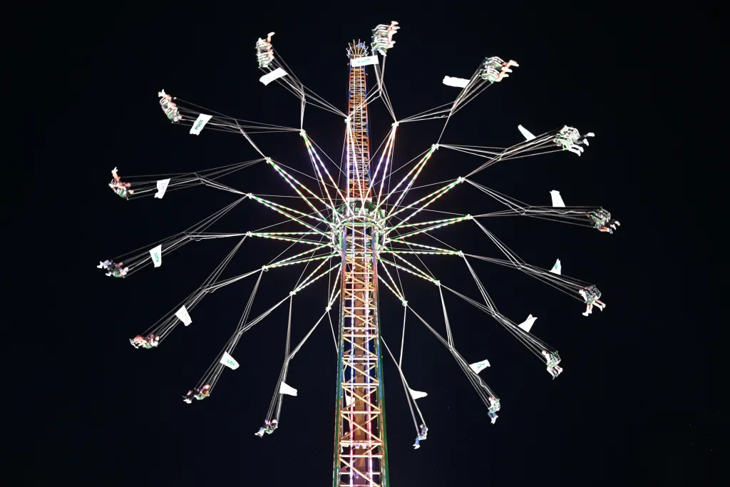 Hoch fliegendes Kettenflieger-Karussell bei Nacht mit Gästen in den Sitzen