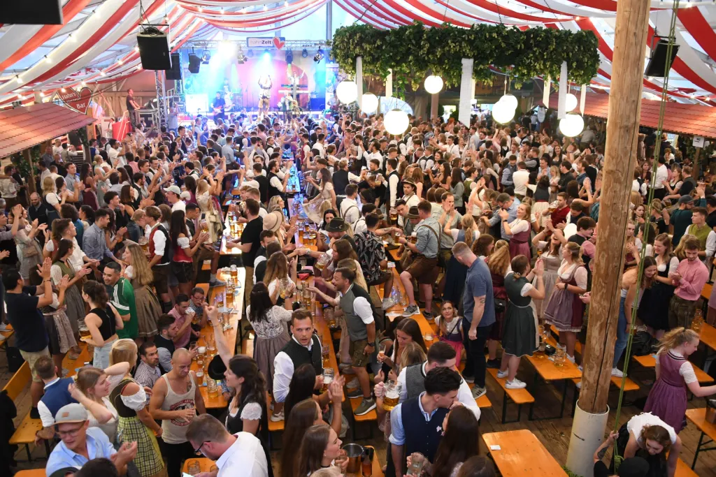 Volles Hahnzelt mit feiernden Gästen vor der Bühne, rot-weißer Zeltdach