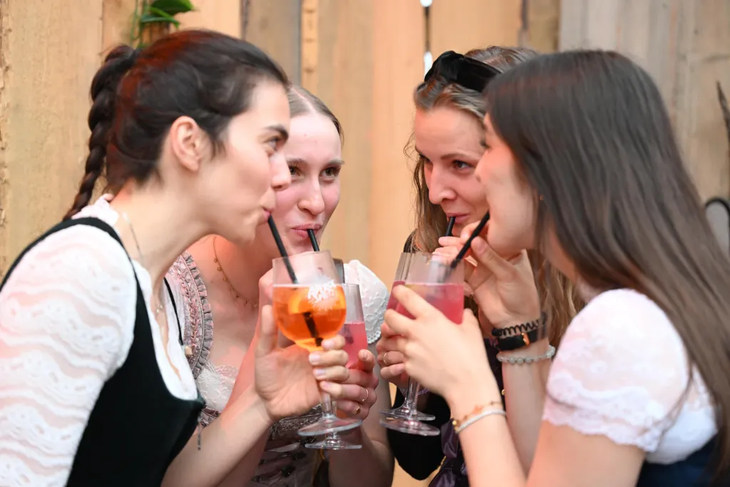 Vier junge Frauen trinken gemeinsam Aperol- und Beerencocktails mit Strohhalmen